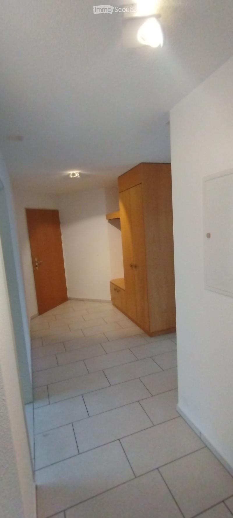 Empty hallway with tiled floor, white walls, and a wooden cabinet on the right side.
