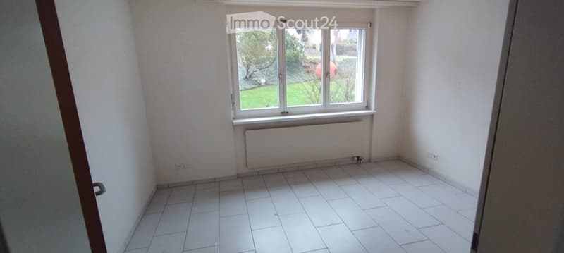 Empty room with white tiled flooring, white walls, a window with white frame, and a radiator below the window. No furniture or equipment is present.
