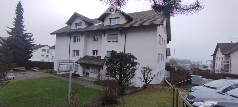 Two-story house with white exterior, multiple windows, garage, and parking area.