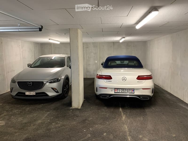 Underground garage with two parked cars, concrete walls, and fluorescent lighting.