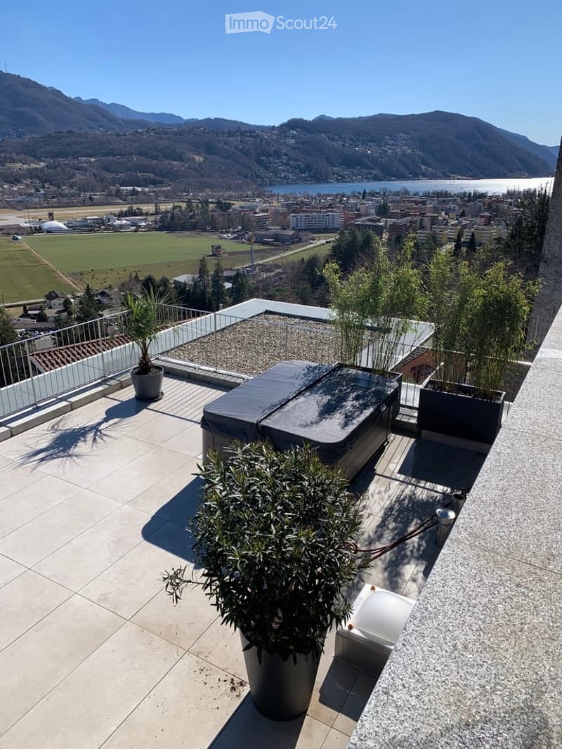 Rooftop terrace with a hot tub, potted plants, and a panoramic view of a lake and mountains.