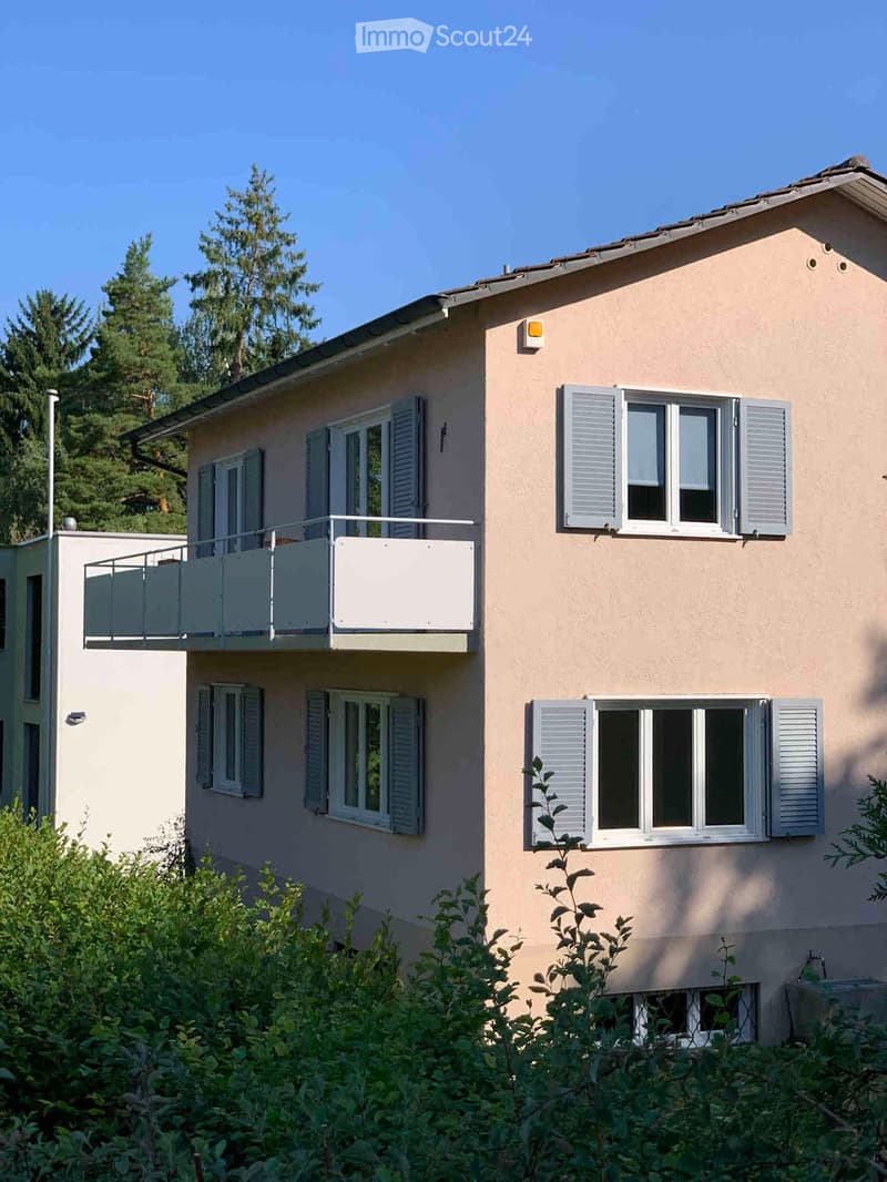 Two-story house with beige exterior, multiple windows with shutters, and a balcony on the upper level.