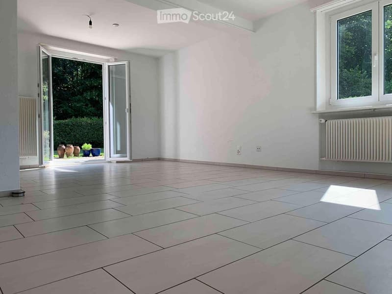 Empty room with tiled floor, white walls, large windows, and sliding glass doors leading to an outdoor area.