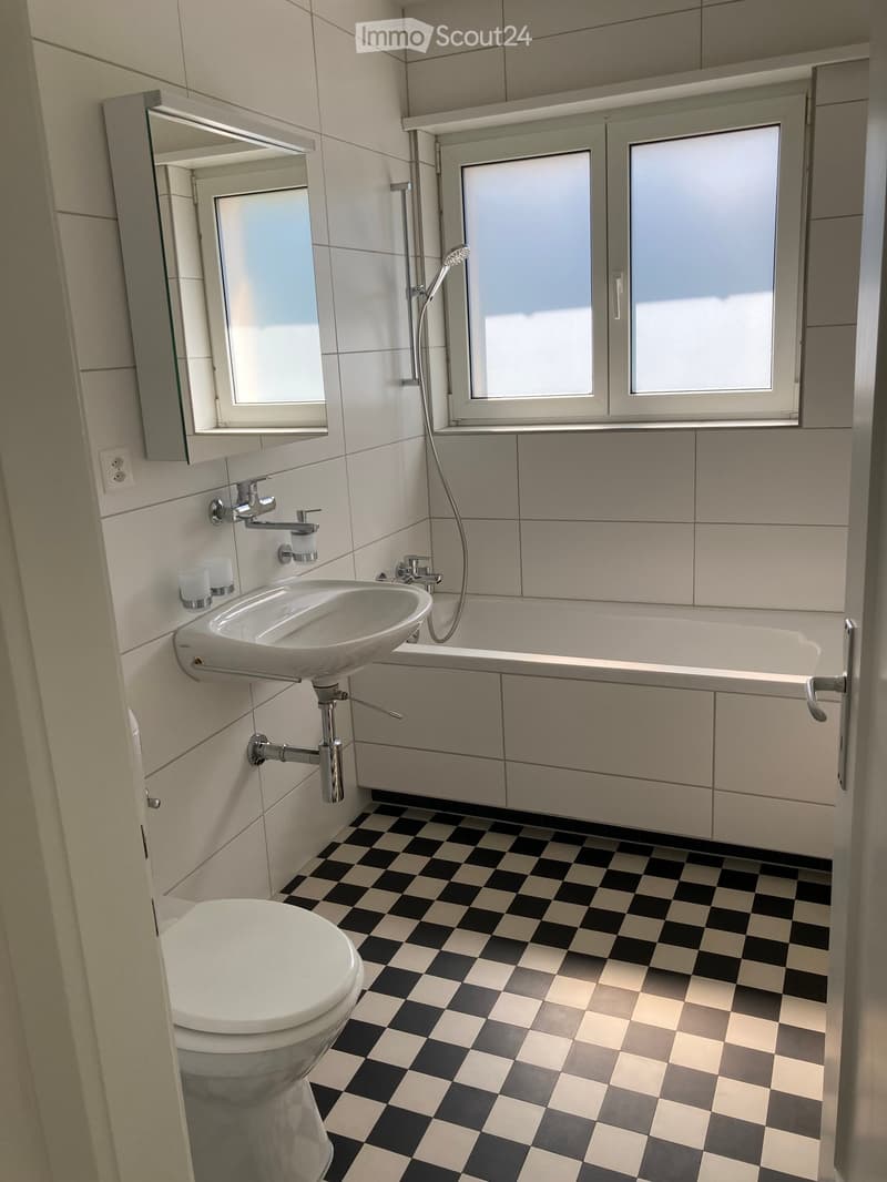 Modern bathroom with white tiles, black and white checkered floor, toilet, sink, bathtub, and mirror.