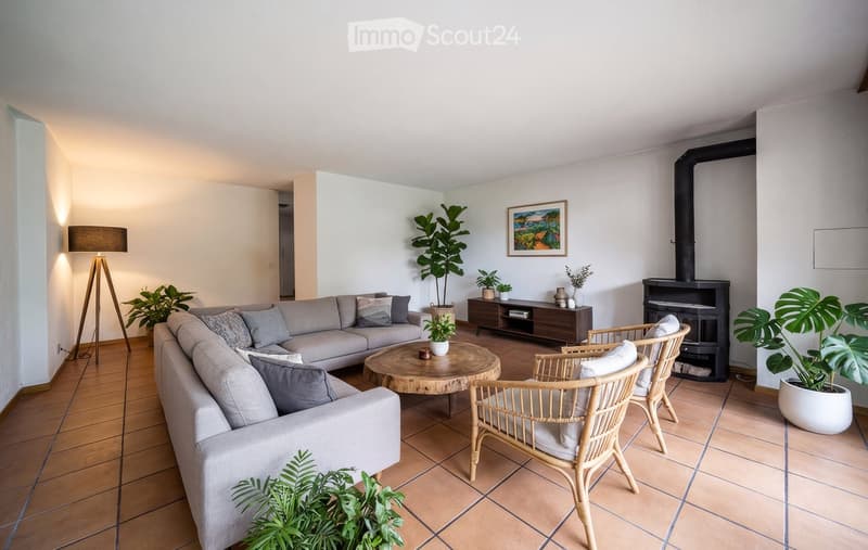 Modern living room with a grey sectional sofa, wooden coffee table, wicker chairs, floor lamp, fireplace, and decorative plants.