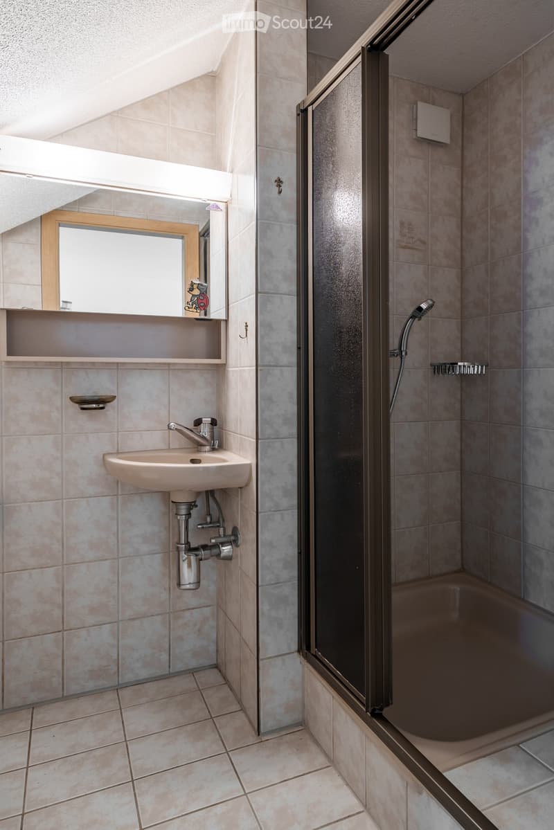 Bathroom with a sink, mirror, and a walk-in shower with a glass door. The walls and floor are tiled in a light beige color.