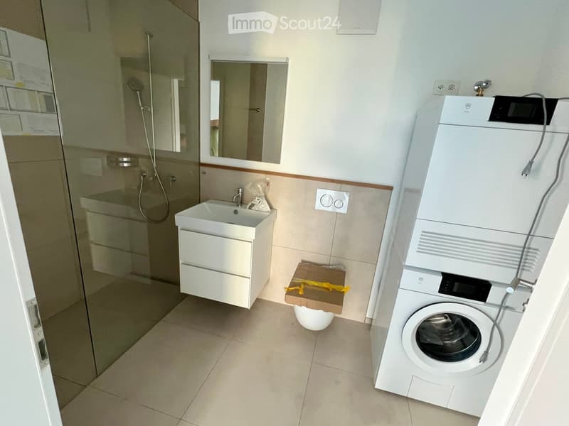 Modern bathroom with a white sink, mirror, glass-enclosed shower, and a stacked washer/dryer unit.