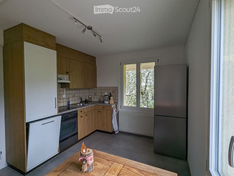 Modern kitchen with wooden cabinets, stainless steel appliances, granite countertop, and a small wooden table with a decorative centerpiece.
