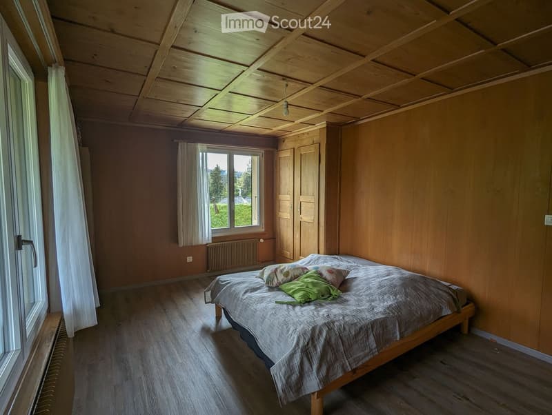 Cozy wooden bedroom with a single bed, pillows, a wardrobe, and large windows offering a scenic view.
