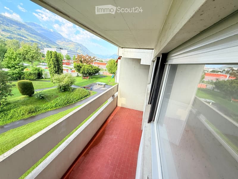 Balcony with red brick tiles, overlooking a green park and distant mountains.