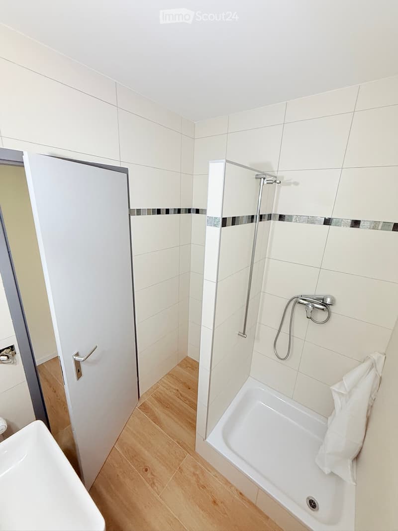 Modern bathroom with white tiled walls, a bathtub, a shower area, and a towel on the edge of the tub.