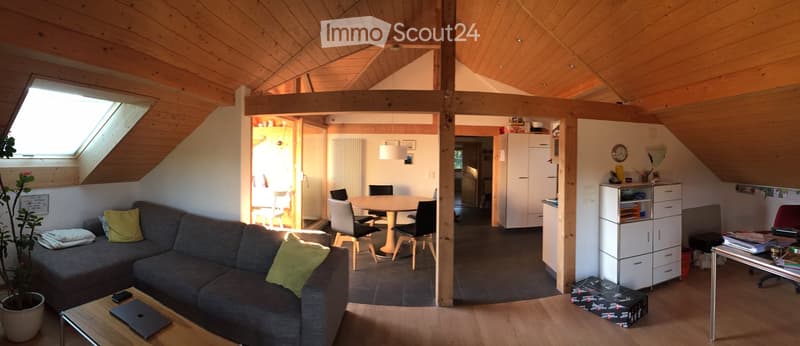 Bright, wooden-floored living space with a grey sofa, coffee table, laptop, dining area with chairs and table, potted plant, and kitchen area with cabinets and fridge.