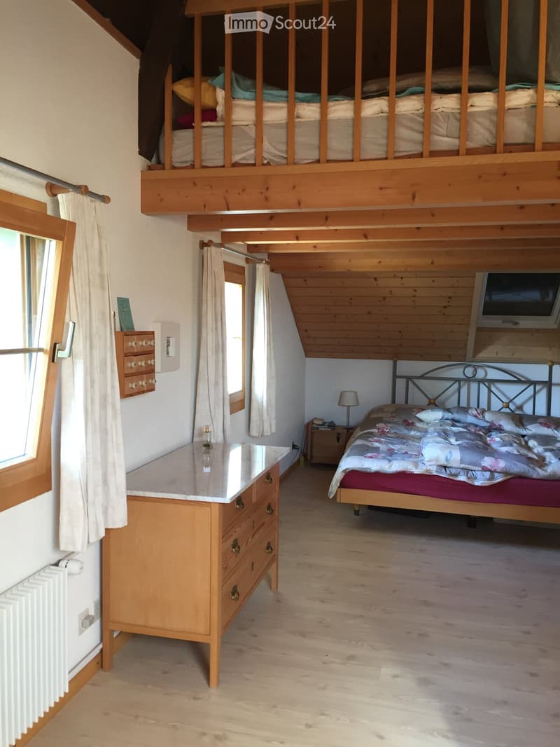 Cozy bedroom with wooden floors, a double bed with floral bedding, a nightstand with a lamp, a wooden dresser with a marble top, and a lofted twin-sized bed above.