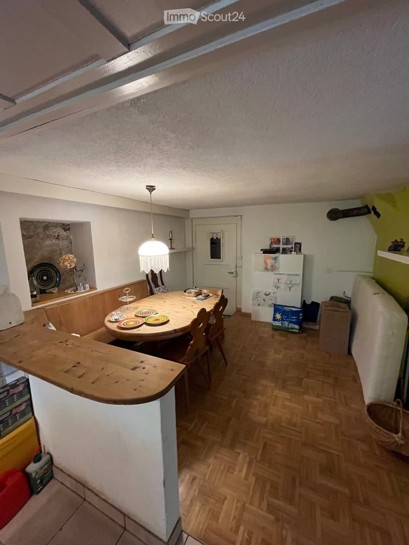 A cozy dining area with a wooden dining table, chairs, and a refrigerator, featuring a wooden floor and a hanging light fixture.