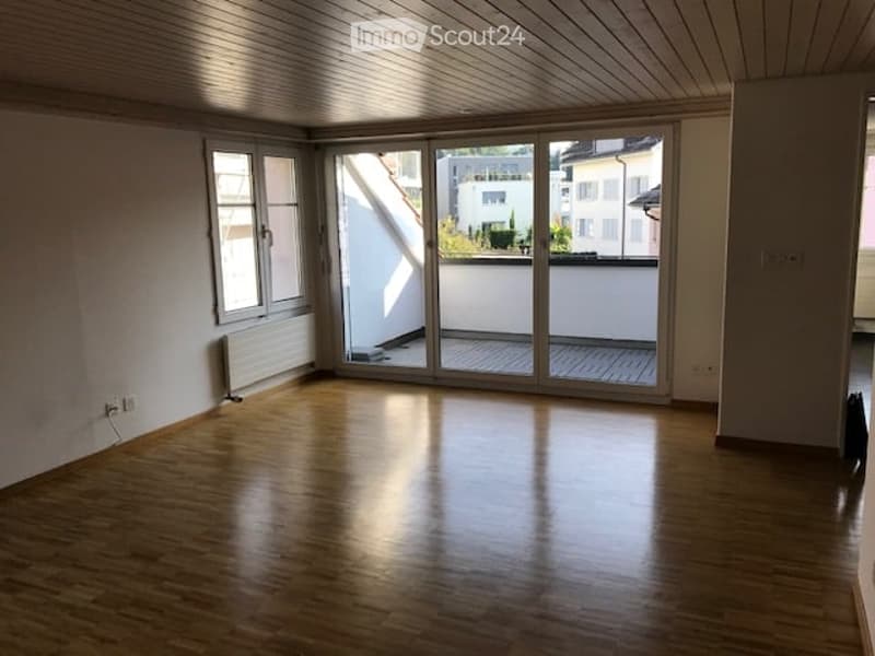 Empty room with wooden flooring, large sliding glass doors leading to a balcony, and white walls.