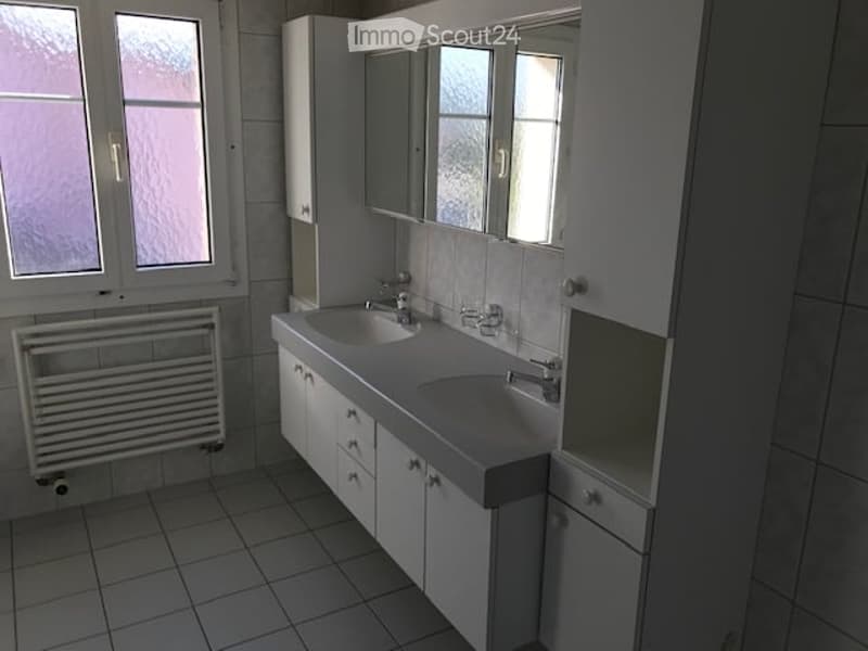 Modern bathroom with two sinks, white cabinets, tiled walls and floor, and a radiator below the window.