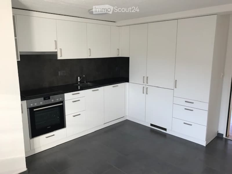 Modern kitchen with white cabinets, black countertops, and a built-in oven. Features a sleek, minimalist design with a dark tiled floor.