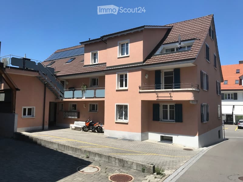 Two-story house with pink exterior, multiple windows, balconies, solar panels on the roof, and a parked motorcycle.