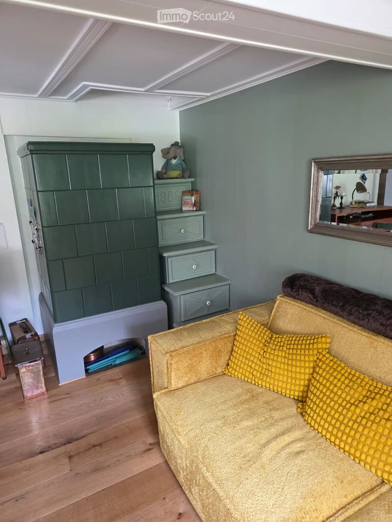 Living room with a yellow sofa, patterned pillows, a green cabinet, a mirror, and a small stool.