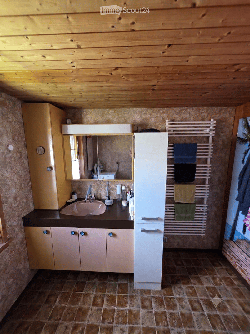 Bathroom with wooden ceiling, tiled floor, sink, mirror, cabinet, and towel rack with towels.