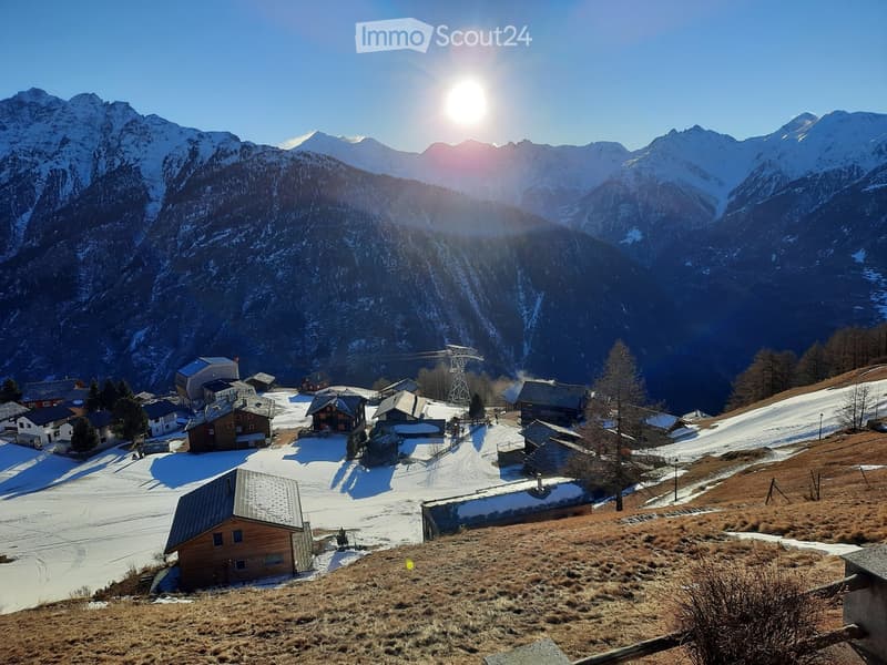 A picturesque mountain village with snow-covered peaks in the background, featuring scattered houses and a ski lift structure.