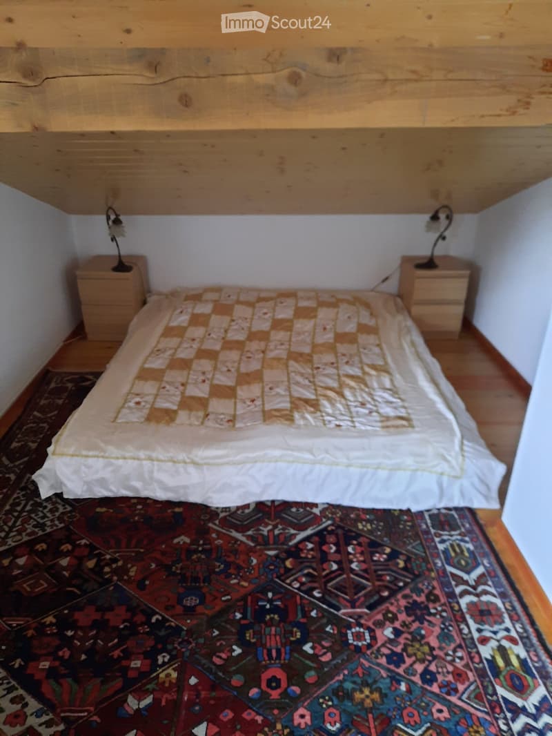 Bedroom with wooden ceiling, two wooden nightstands, a checkered bedspread, wooden floor, and two lamps.