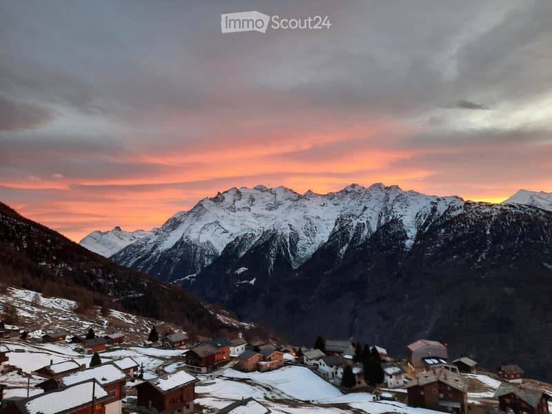 A snowy mountain range with houses scattered on the lower slopes and clear sky with sunset colors