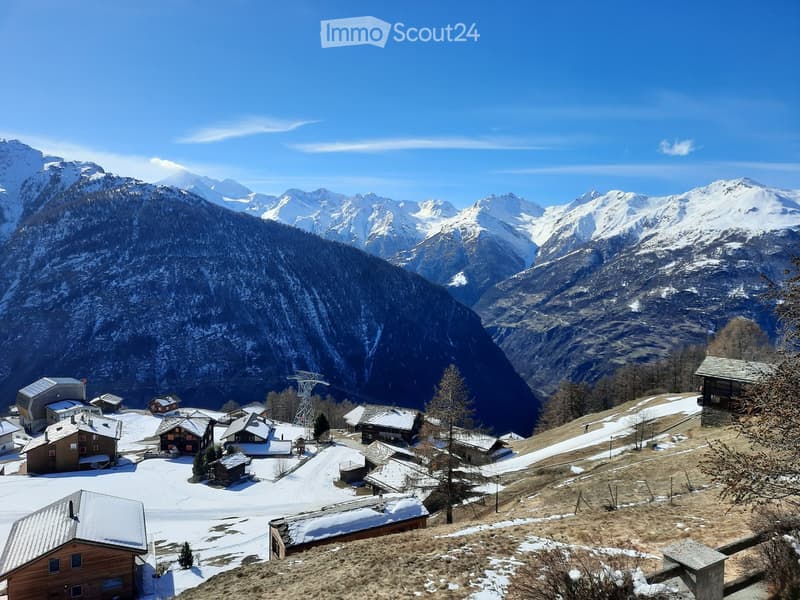 A cluster of houses and buildings in a snowy mountain valley, surrounded by snow-covered peaks and trees.