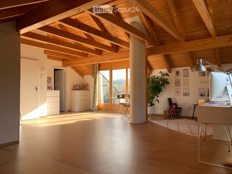 Bright, open room with wooden beams, hardwood floor, large windows, desk, chair, small table, plant, and cabinets.