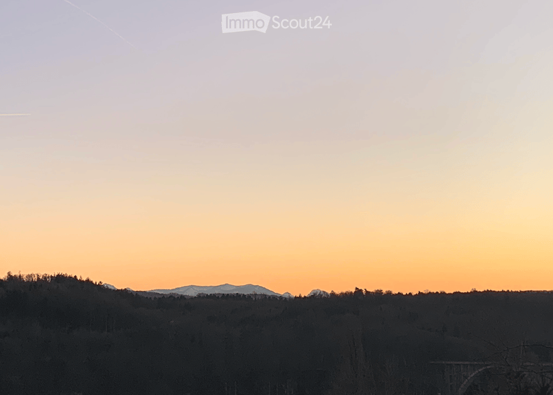 A serene view of a forested landscape at sunset, with mountains visible in the distance.