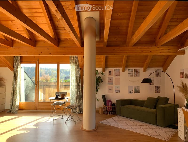 Bright living room with wooden beams, large windows, green sofa, small table with chairs, floor lamp, and decorative picture frames on the wall.