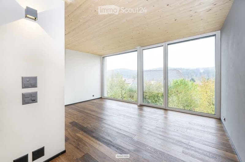 Empty room with wooden flooring, white walls, large windows offering a scenic view, and exposed wooden ceiling beams.
