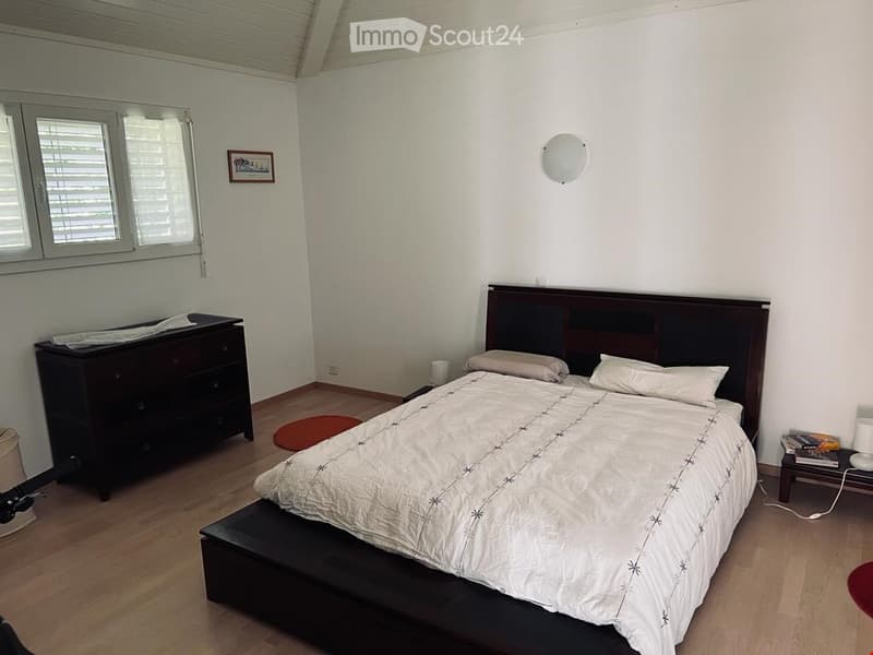 A bedroom with a double bed, nightstands, a dresser, a round rug, a picture frame, and a wall lamp