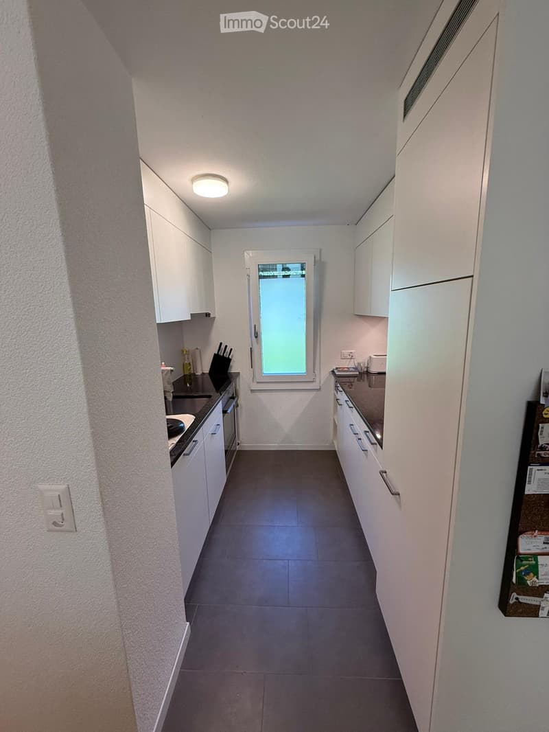 Modern kitchen with white cabinets, stainless steel appliances, and a central island. Features an oven, sink, and a small window with frosted glass.