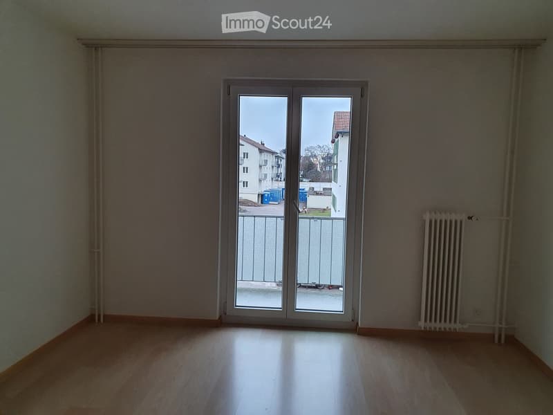 Empty room with wooden flooring, white walls, and a large sliding glass door leading to a balcony.
