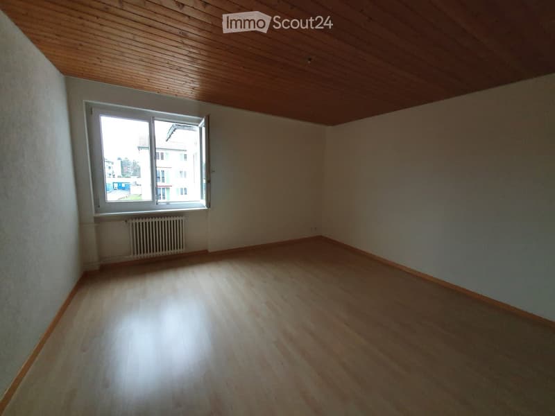 Empty room with wooden flooring, white walls, and a large window with a radiator below it.