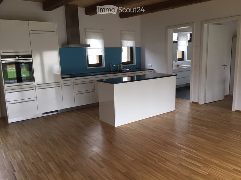 Modern kitchen with white cabinets, a central island, and a stainless steel oven. The floor is made of light wooden planks, and there is a blue accent wall behind the sink.