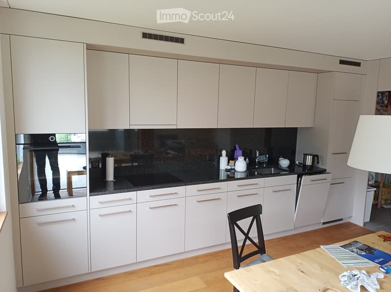 Modern kitchen with white cabinets, black countertop, and stainless steel appliances. Includes a sink, faucet, and a small dining area with a table and chair.