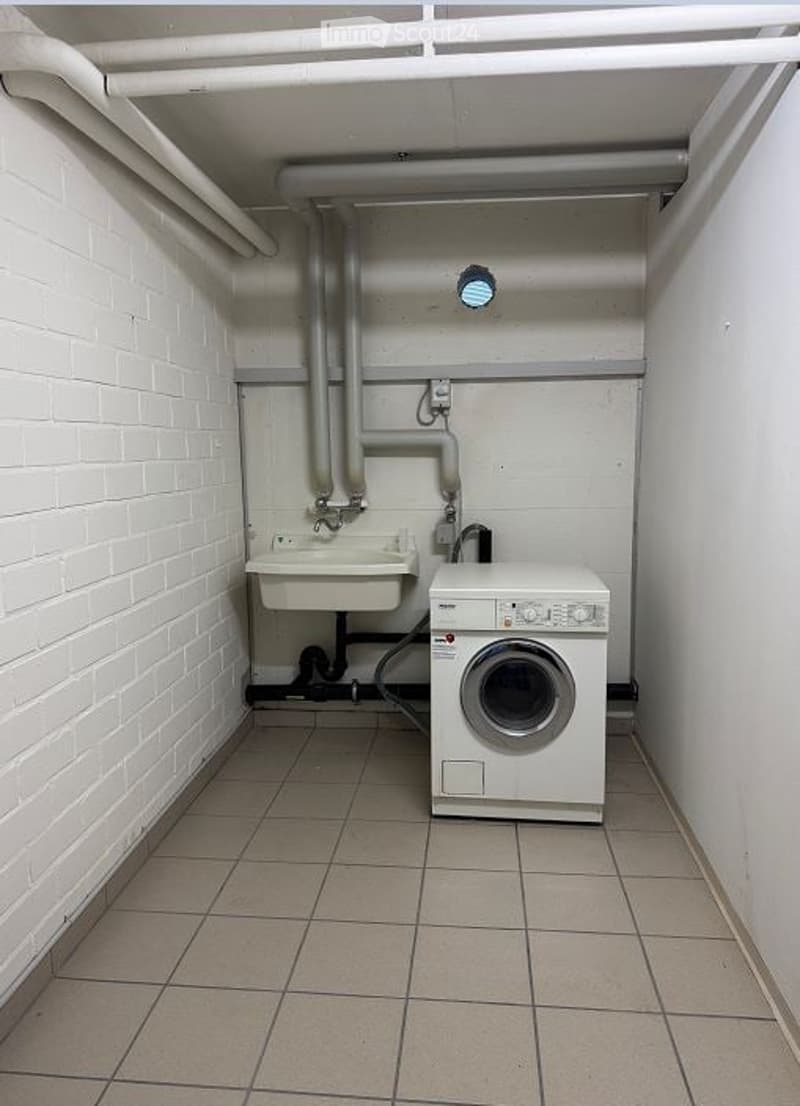 Small bathroom with white brick walls, tiled floor, sink, and washing machine.
