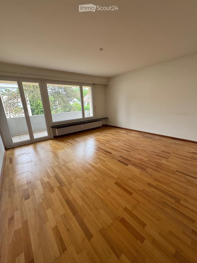 Empty room with wooden flooring, large windows, and a radiator under the windows.
