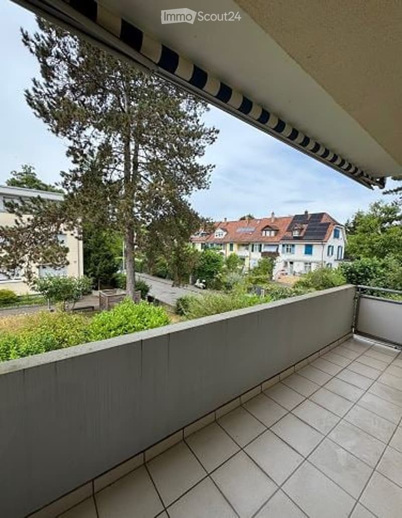 Balcony with tiled floor, railing, and view of a residential area with houses, trees, and a road.