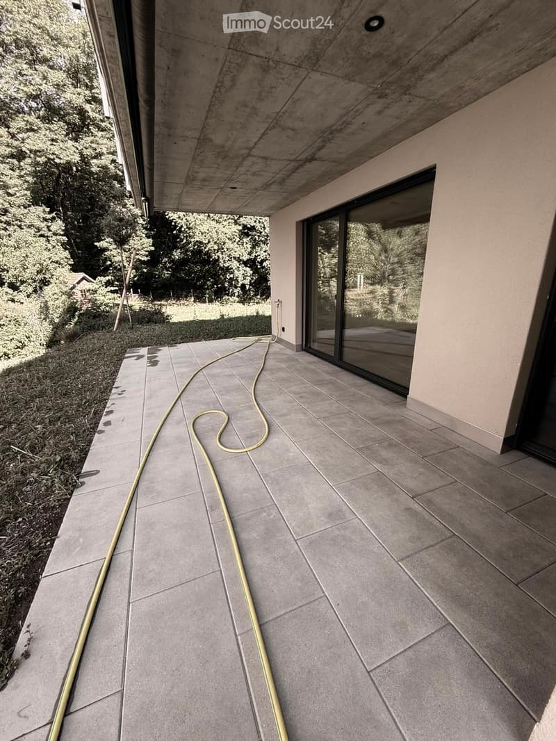 Modern concrete balcony with large glass doors, tiled floor, and a garden view.