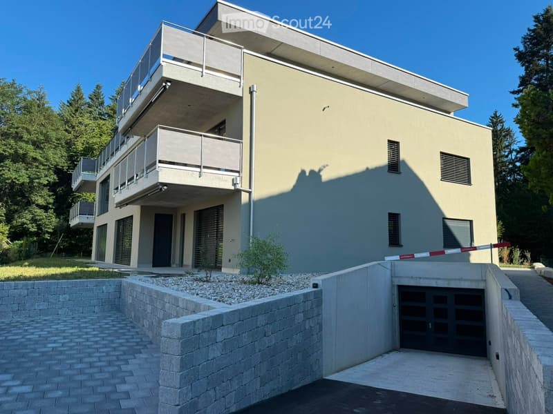 Modern two-story house with light gray facade, multiple balconies, and a garage entrance.