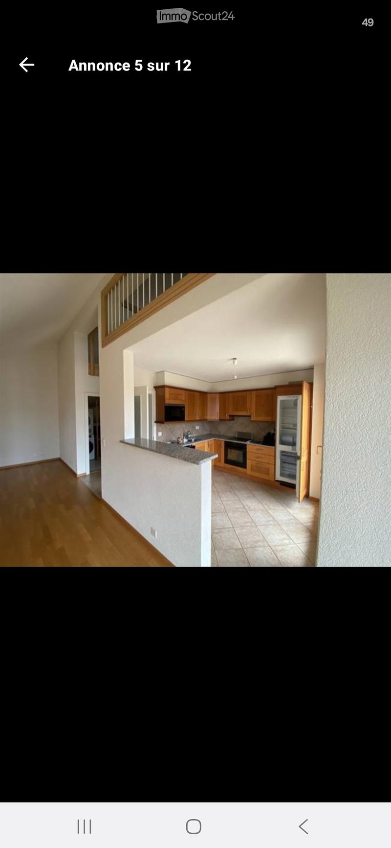 Open-plan kitchen and living area with wooden cabinets, a refrigerator, oven, and a countertop. The living area has wooden flooring and a staircase leading to an upper level.