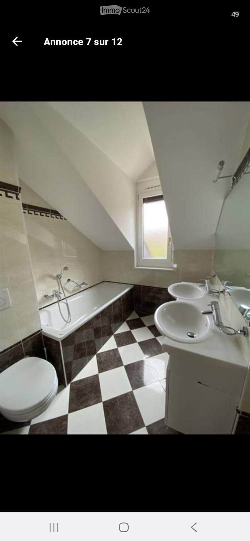 Bathroom with a bathtub, toilet, double sink, and a window letting in natural light. The floor has a black and white checkered tile pattern.