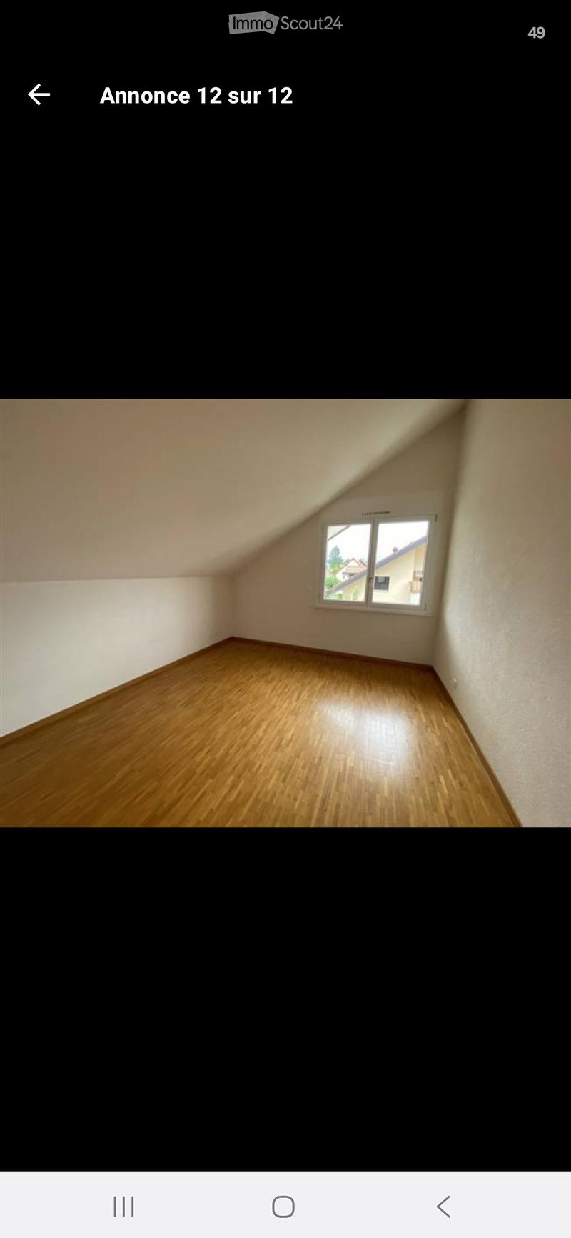 Empty room with wooden flooring and white walls, featuring a single window with a view of neighboring buildings.