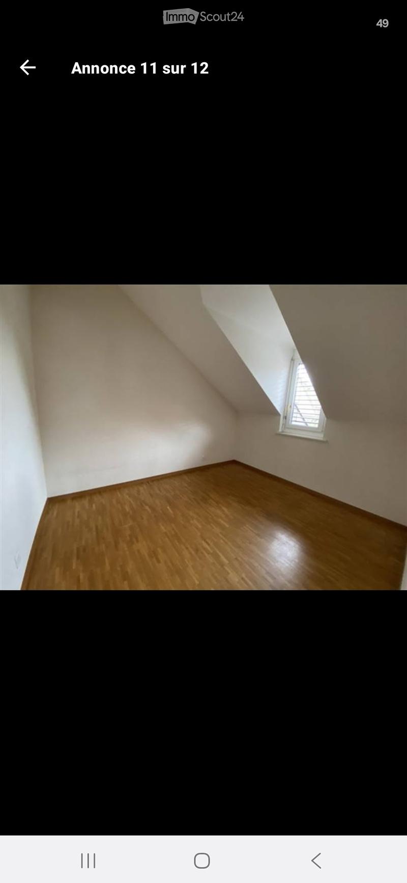 Empty attic room with wooden flooring, white walls, and a single window with blinds.