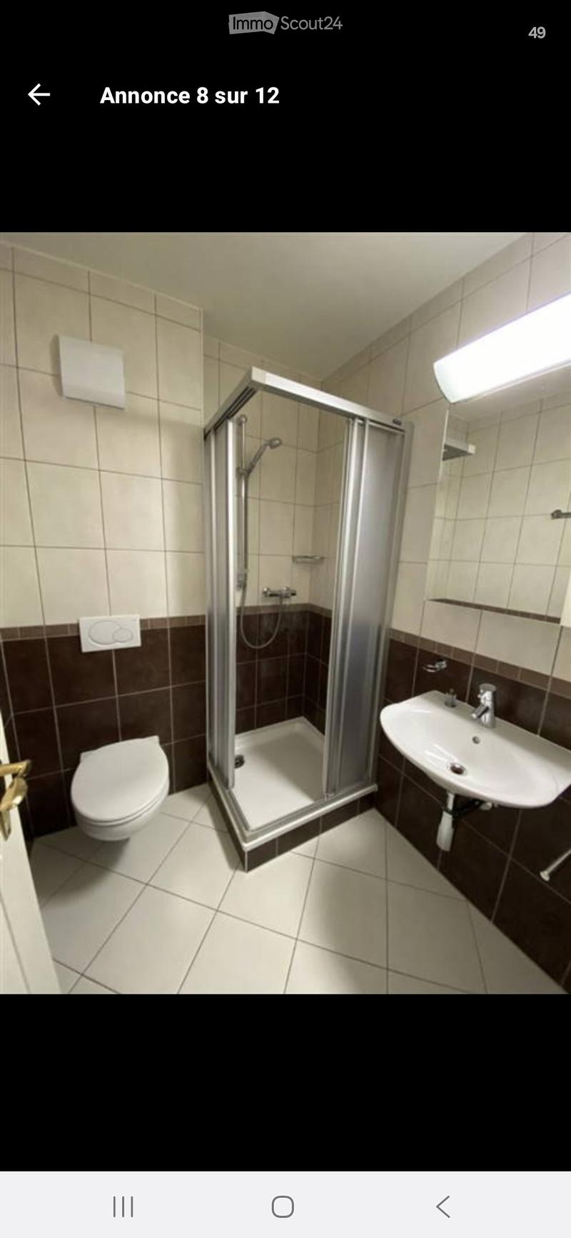Modern bathroom with white tiles, a glass-enclosed shower, a toilet, and a sink with a mirror above it.