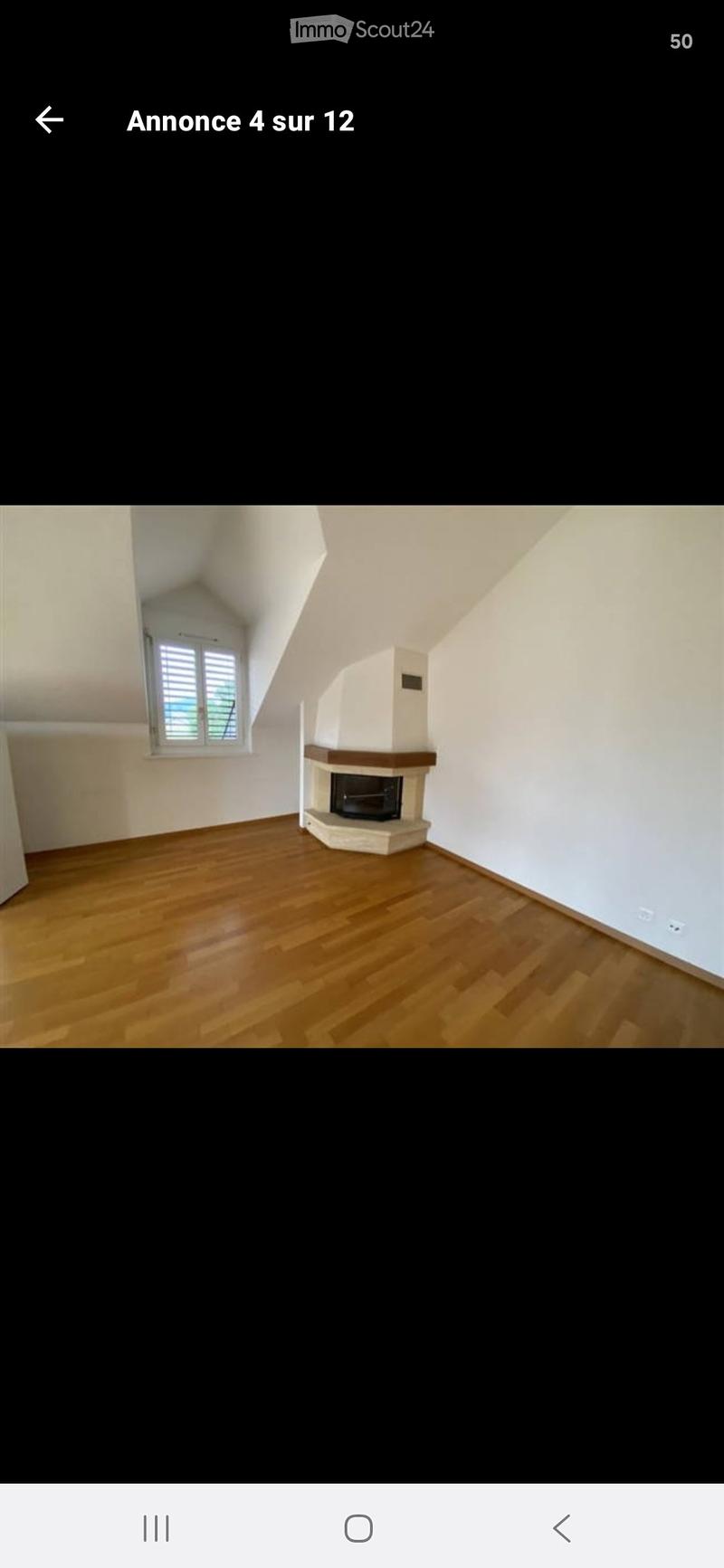 Empty room with wooden flooring, white walls, and a fireplace with a black insert. A window with blinds is visible on one wall.