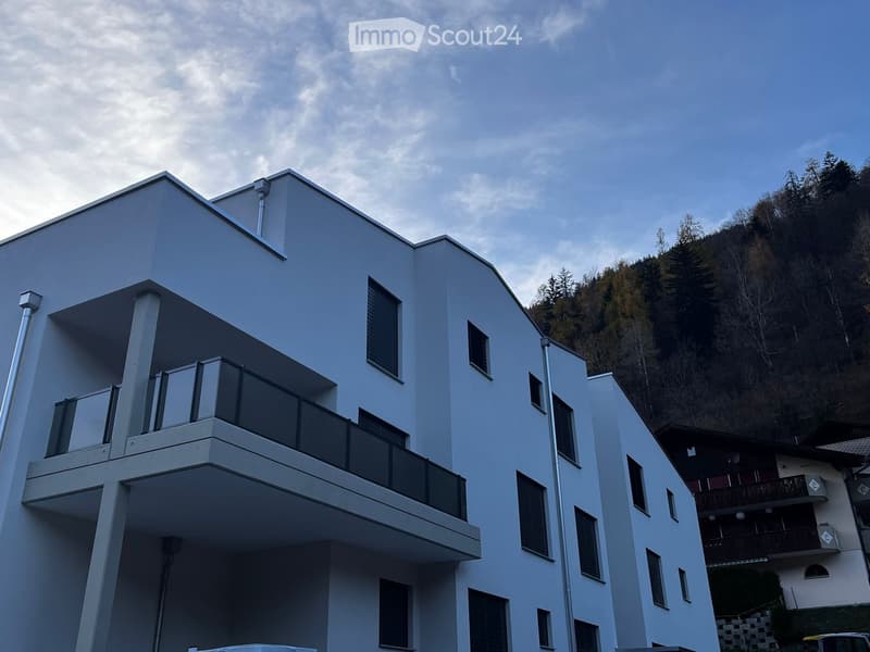 Modern, multi-story building with white exterior and glass balcony on the second floor.